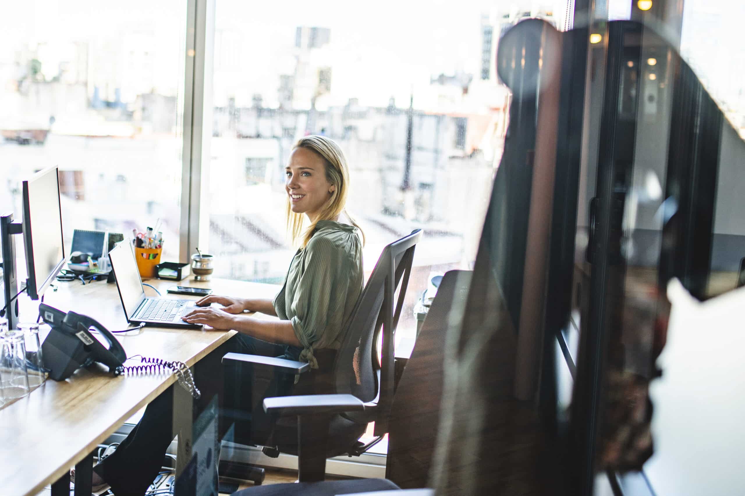 Smiling Blonde Businesswoman Working on Laptop in Office