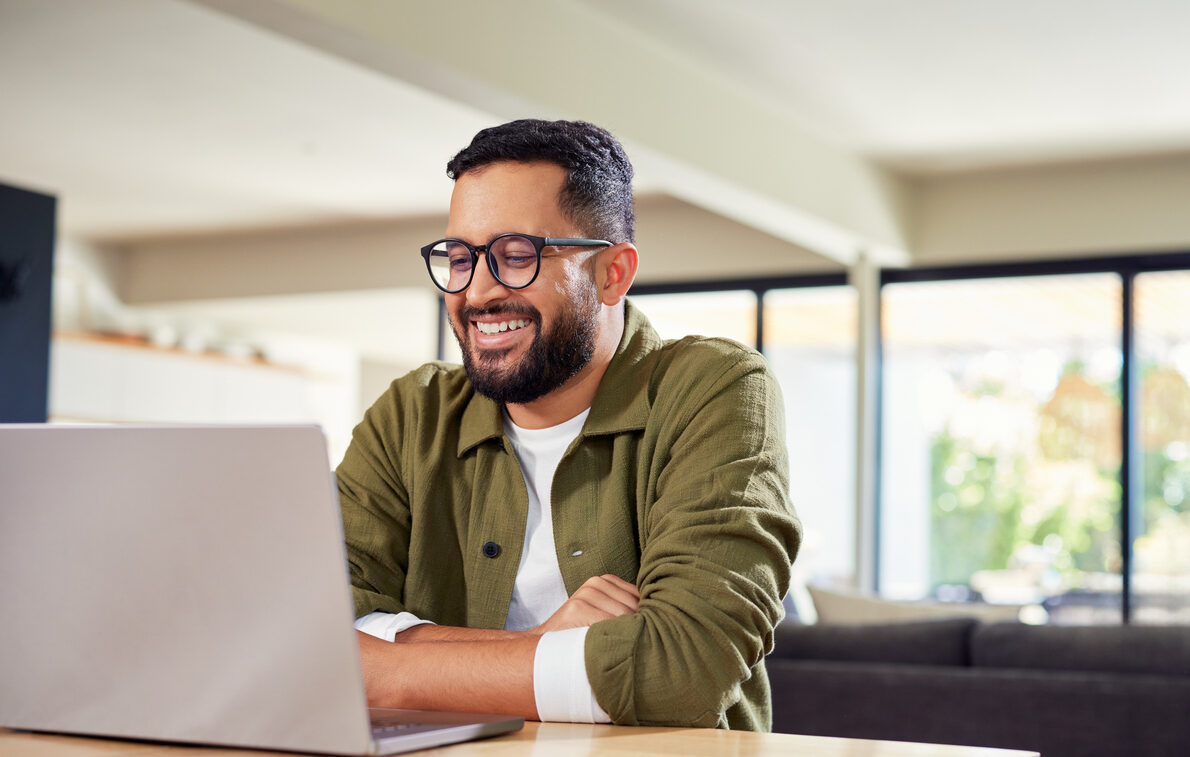 Happy hispanic man working on laptop at home